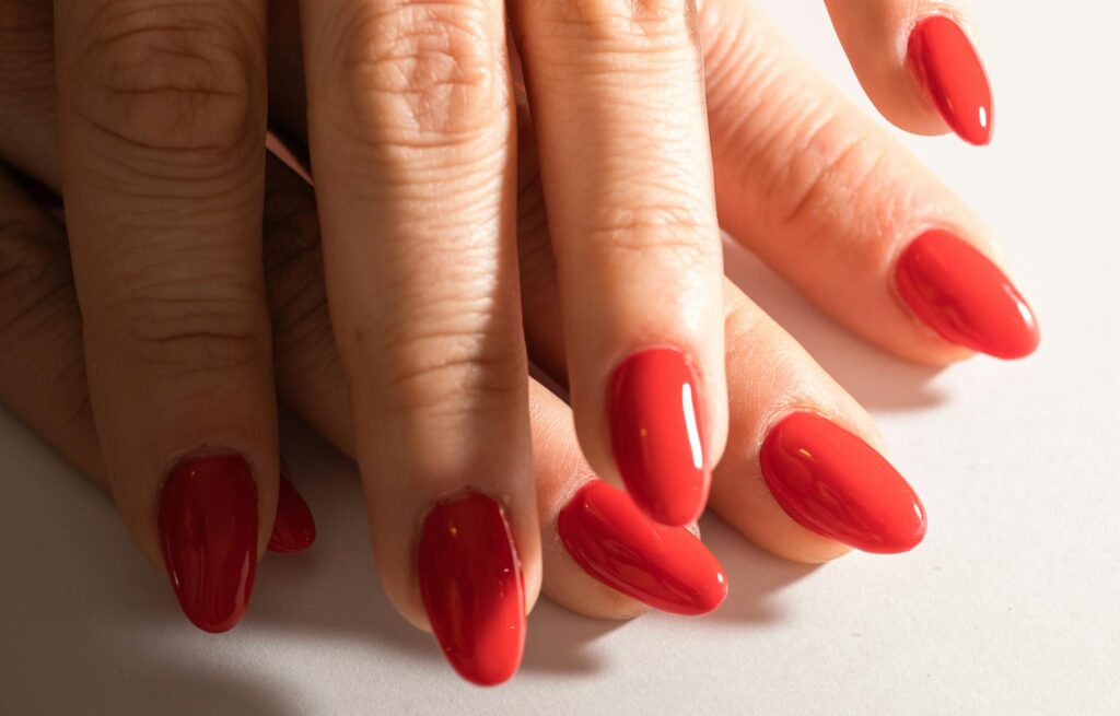 Close-up of female hands with red manicure on white background.