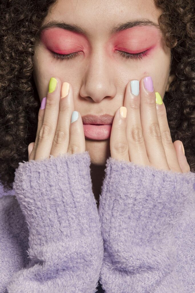 Close-up portrait of a woman with vibrant eyeshadow and pastel manicure, evoking a sense of contemporary style.