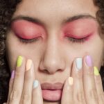 Close-up portrait of a woman with vibrant eyeshadow and pastel manicure, evoking a sense of contemporary style.