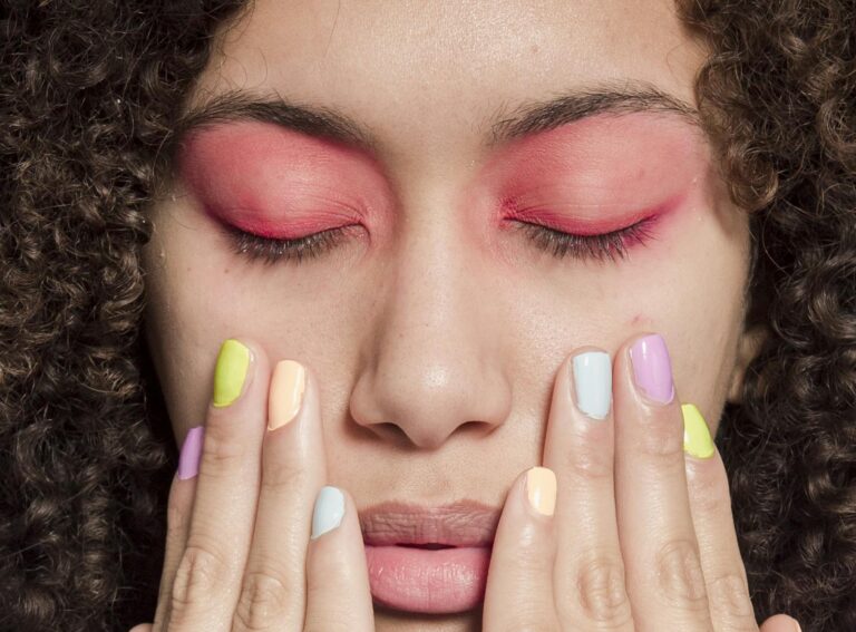 Close-up portrait of a woman with vibrant eyeshadow and pastel manicure, evoking a sense of contemporary style.