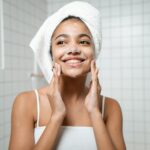 Smiling woman with face wash in a bathroom, embracing self-care and fresh skin.