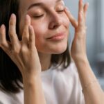 Young woman applying skincare cream with a smile, highlighting self-care and beauty routines.
